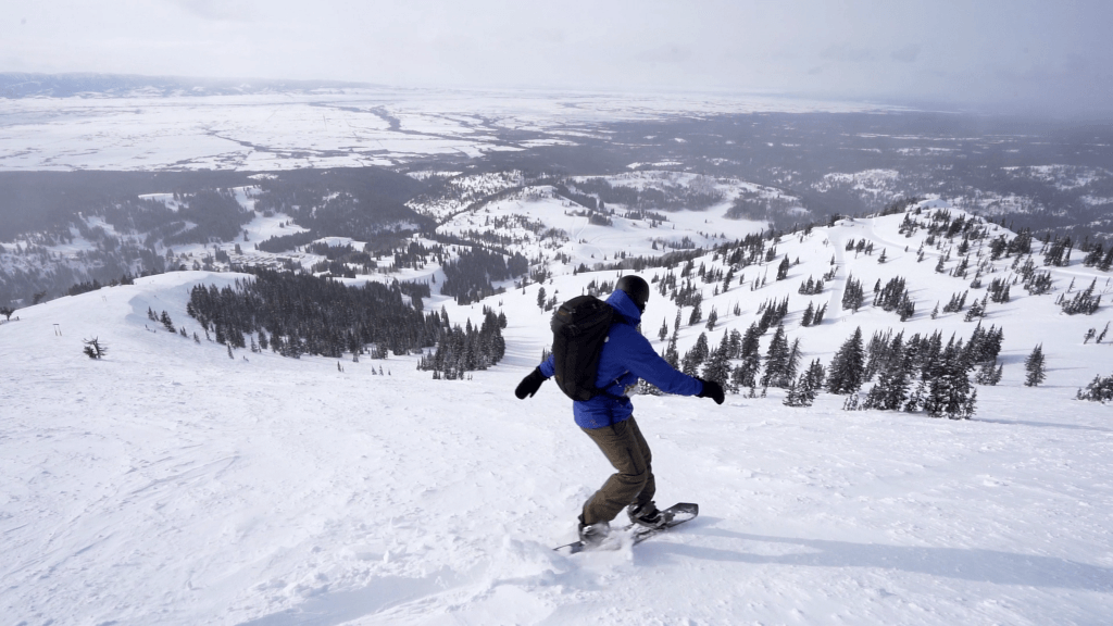 A snowboarder in a blue jacket at the top of a ski run at Grand Targhee Resort.